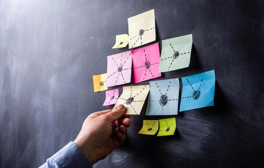 hand pulling sticky note off of blackboard with other sticky notes